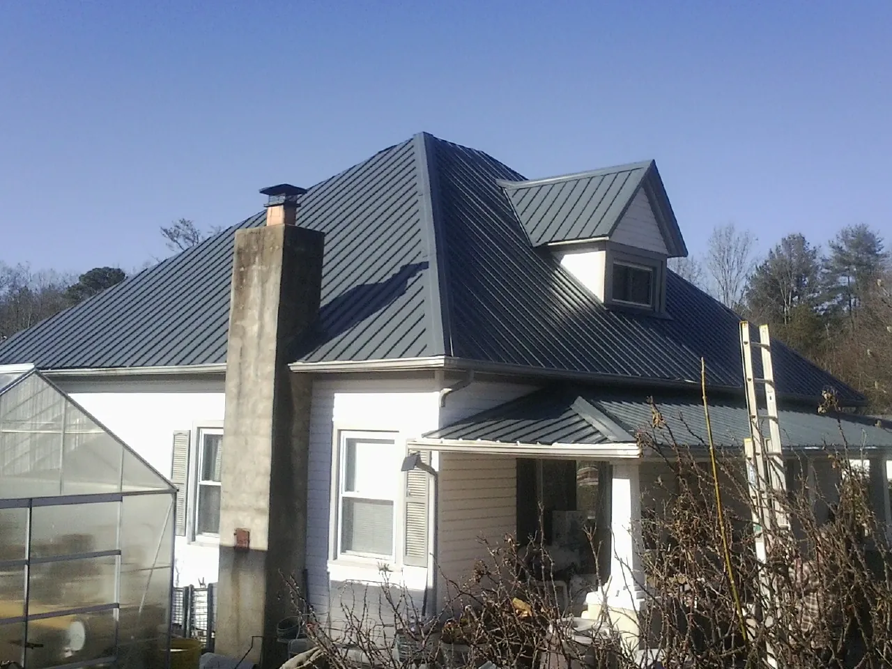 Dark blue standing seam metal roof on a white farmhouse with dormer — Slate & Tile Roof Repair by Roofing Brothers in Queen Anne