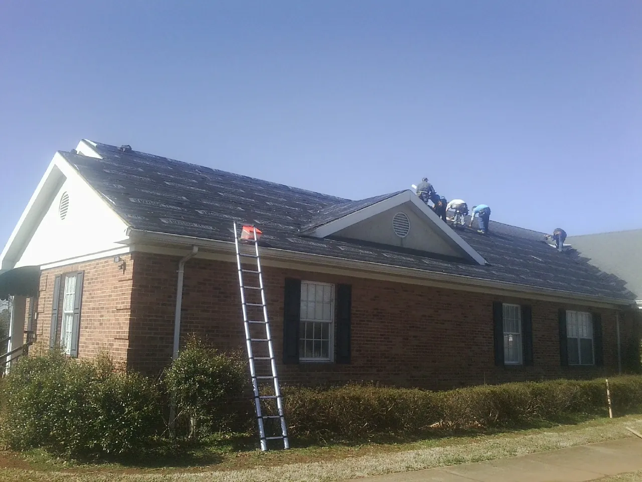 Crew tearing shingles off a brick ranch roof with a ladder set — Emergency Roof Repair work by our crew in Queen Anne