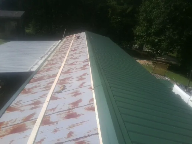 Old rusted panels beside newly installed green metal roofing — Wind Damage Roof Repair by Roofing Brothers in Queen Anne