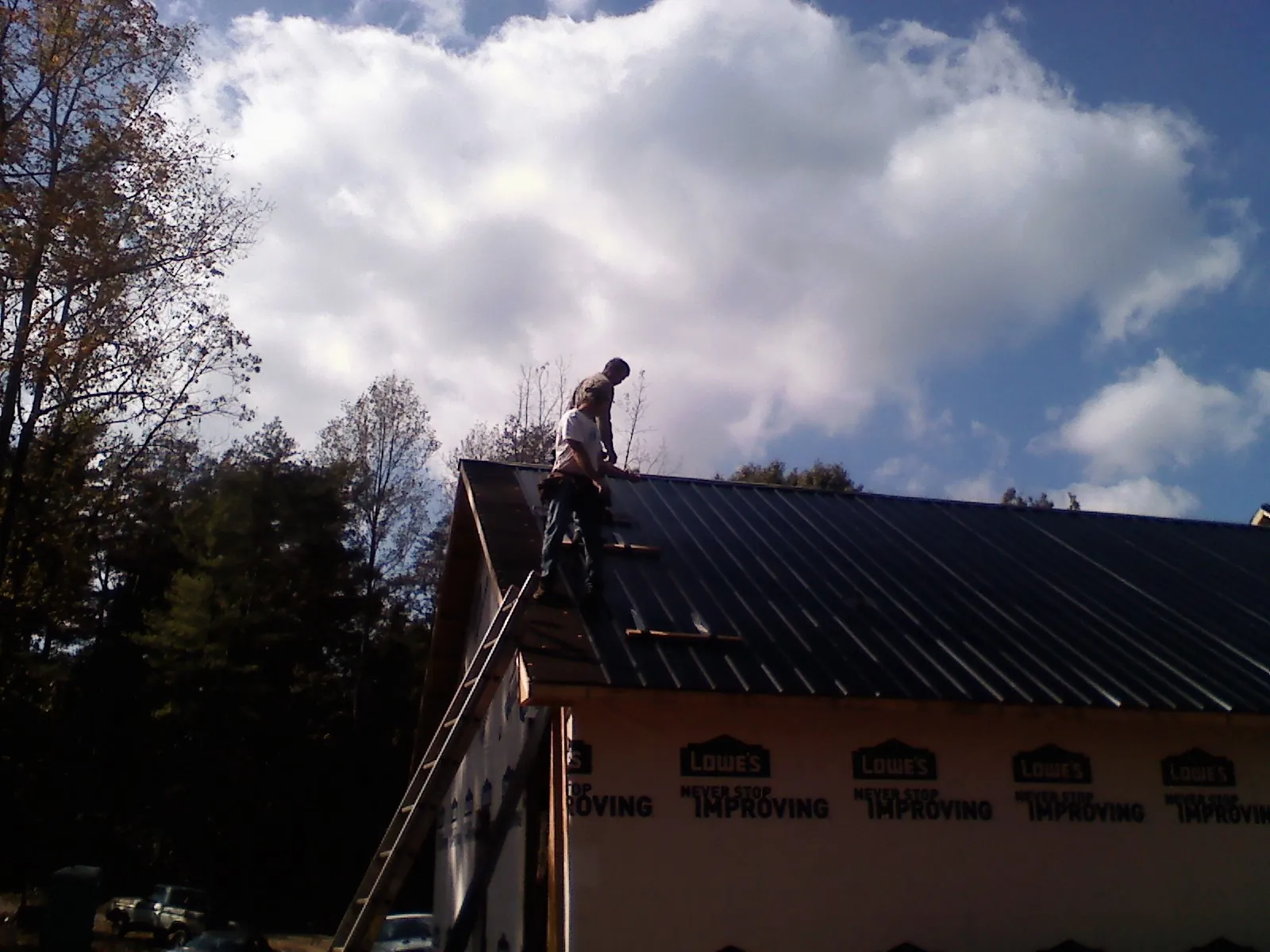 Roofer fastening dark metal panels high against a cloudy sky, from a Roof Inspection job in Queen Anne