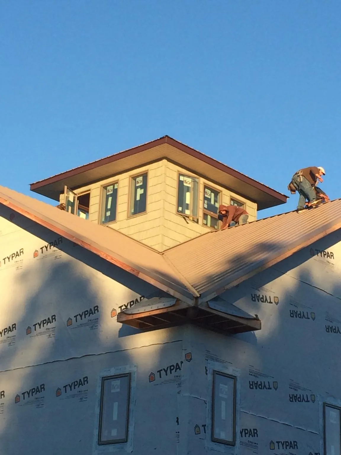Roofers working around a rooftop cupola on a new metal roof at sunset in Queen Anne